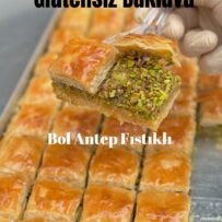 Üzeri altın sarısı renginde kızarmış, kat kat ince hamurlu ve bol Antep fıstıklı kare kesim glutensiz baklava dilimleri
